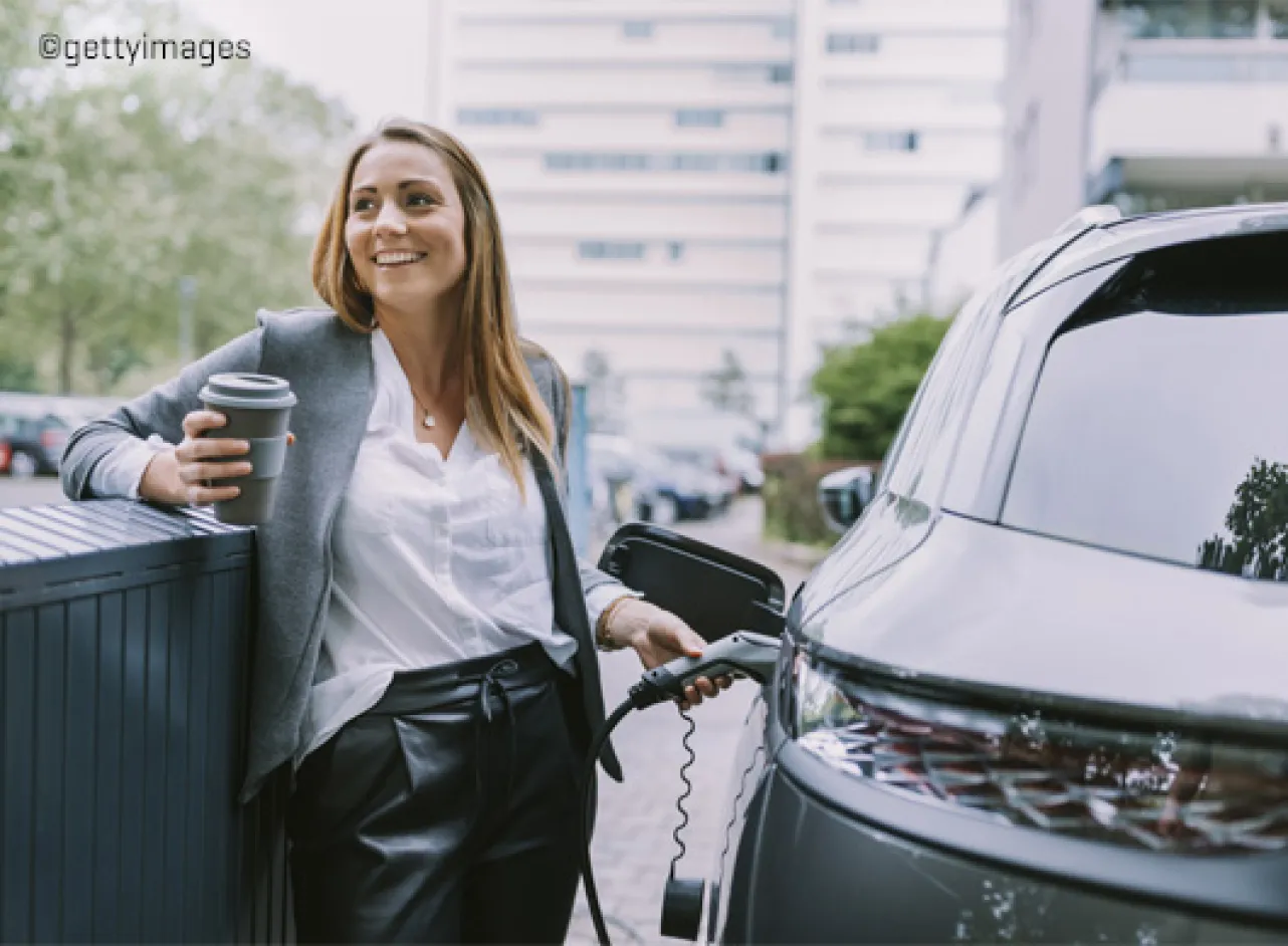 Meisje laad electrische wagen op met koffie in de andere hand